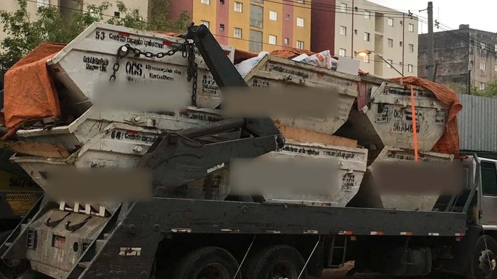 Caminhão carregado com várias caçambas em pátio urbano
